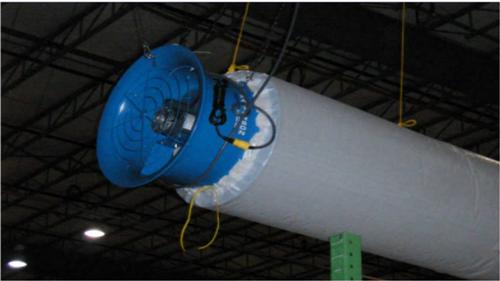 Blue inline fan mounted on a large white fabric duct suspended from a warehouse ceiling.